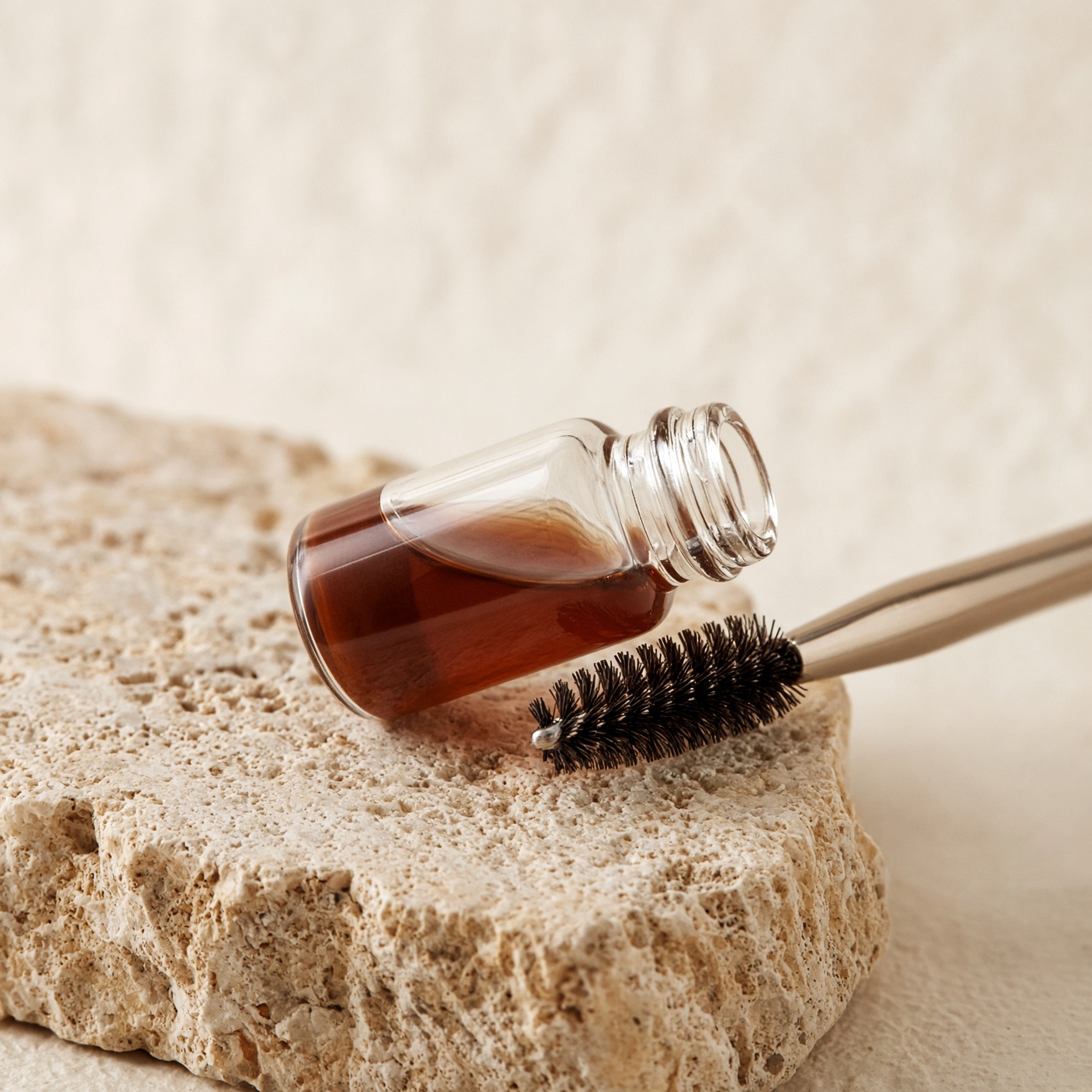 A vial of brown pigment and a spoolie on warm stone